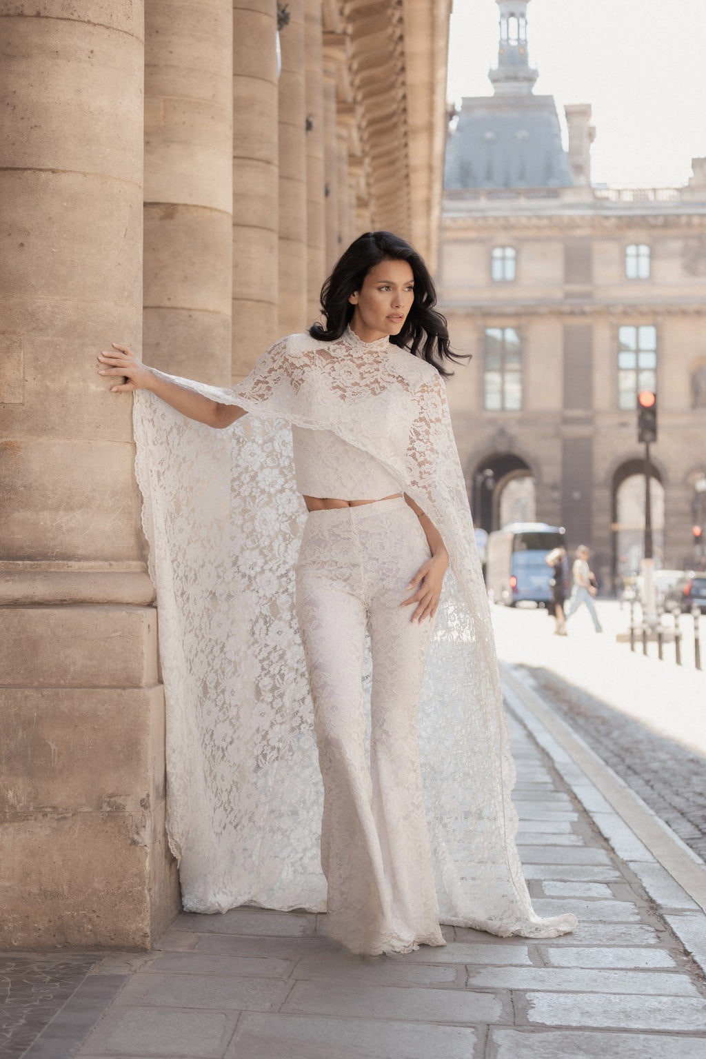 White Chantilly lace wide-leg Femme Pants with the matching lace cape, side view among classical columns.