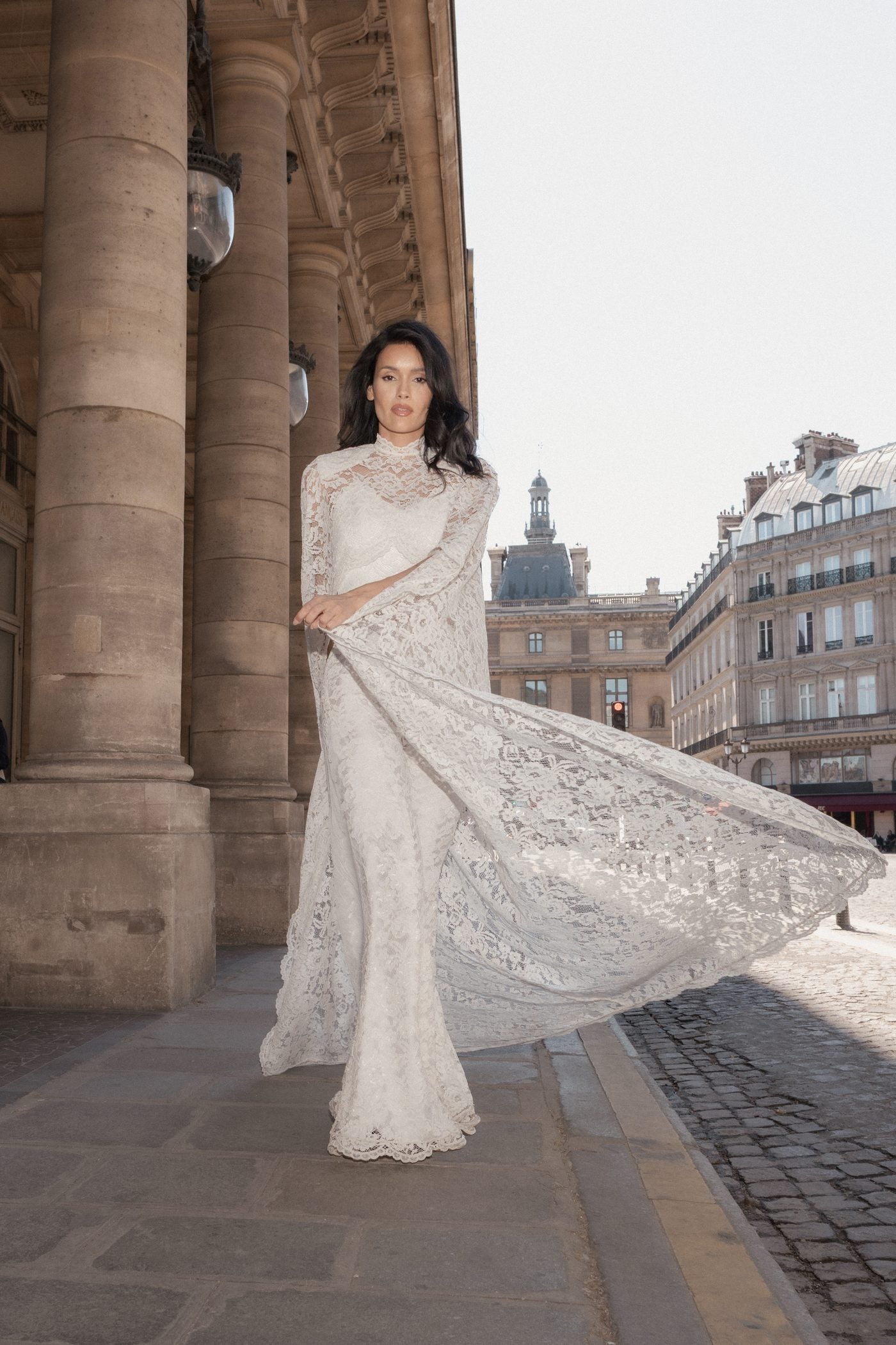 Model turning in a long white Chantilly lace cape under the Palais-Royal colonnade